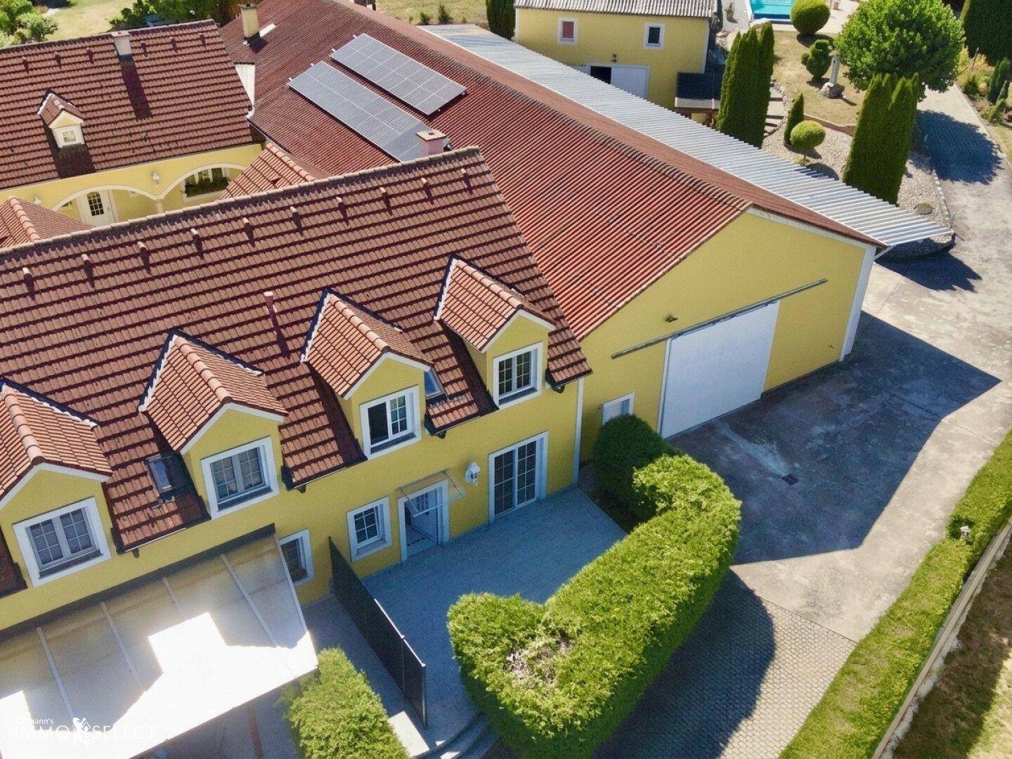 Weitläufige Luftaufnahme des Anwesens mit gelbem Haus, Terrasse und Photovoltaikanlage.