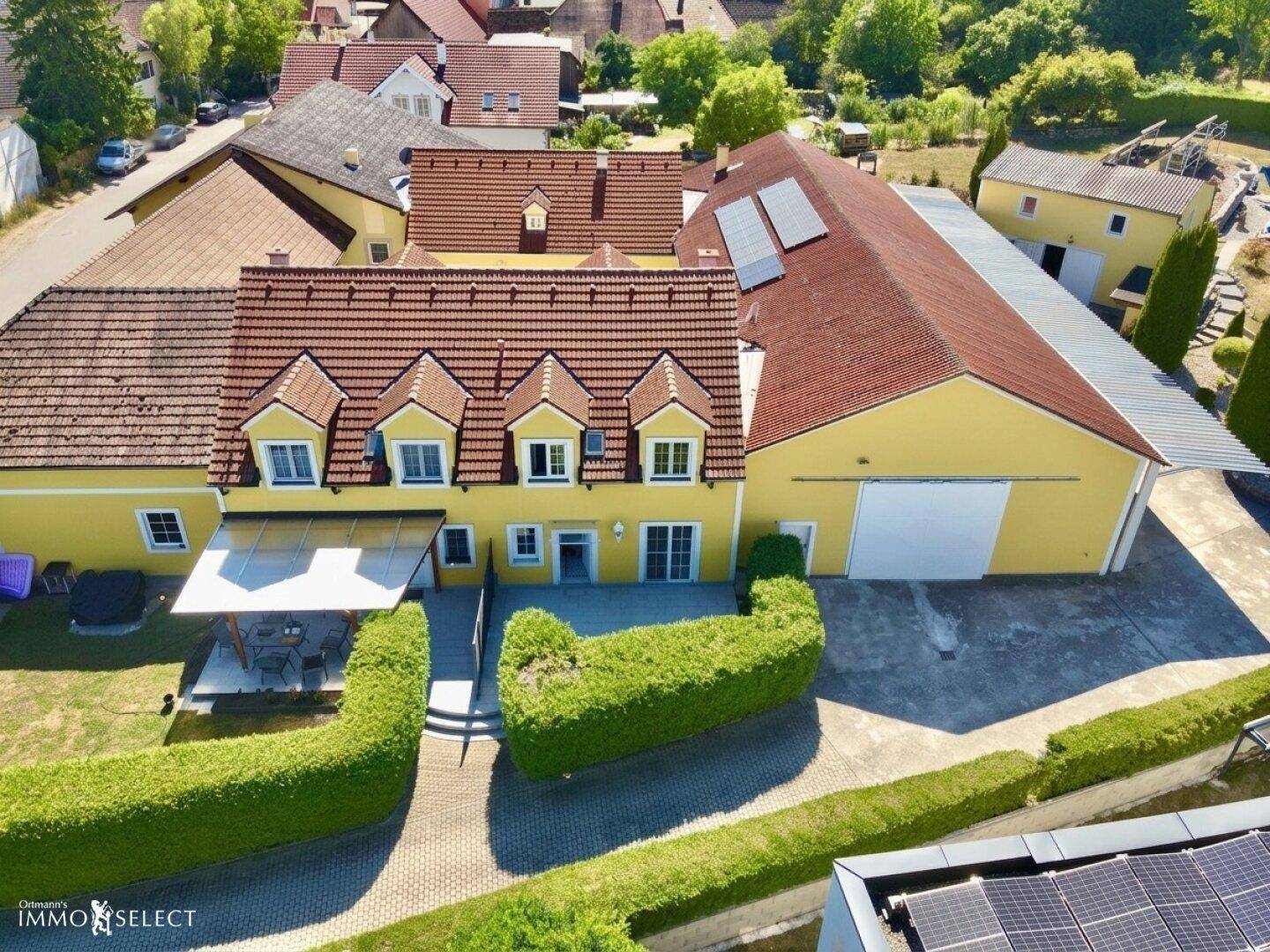 Luftaufnahme des gelben Hauses mit großer Terrasse, Carport und angrenzendem Feld.