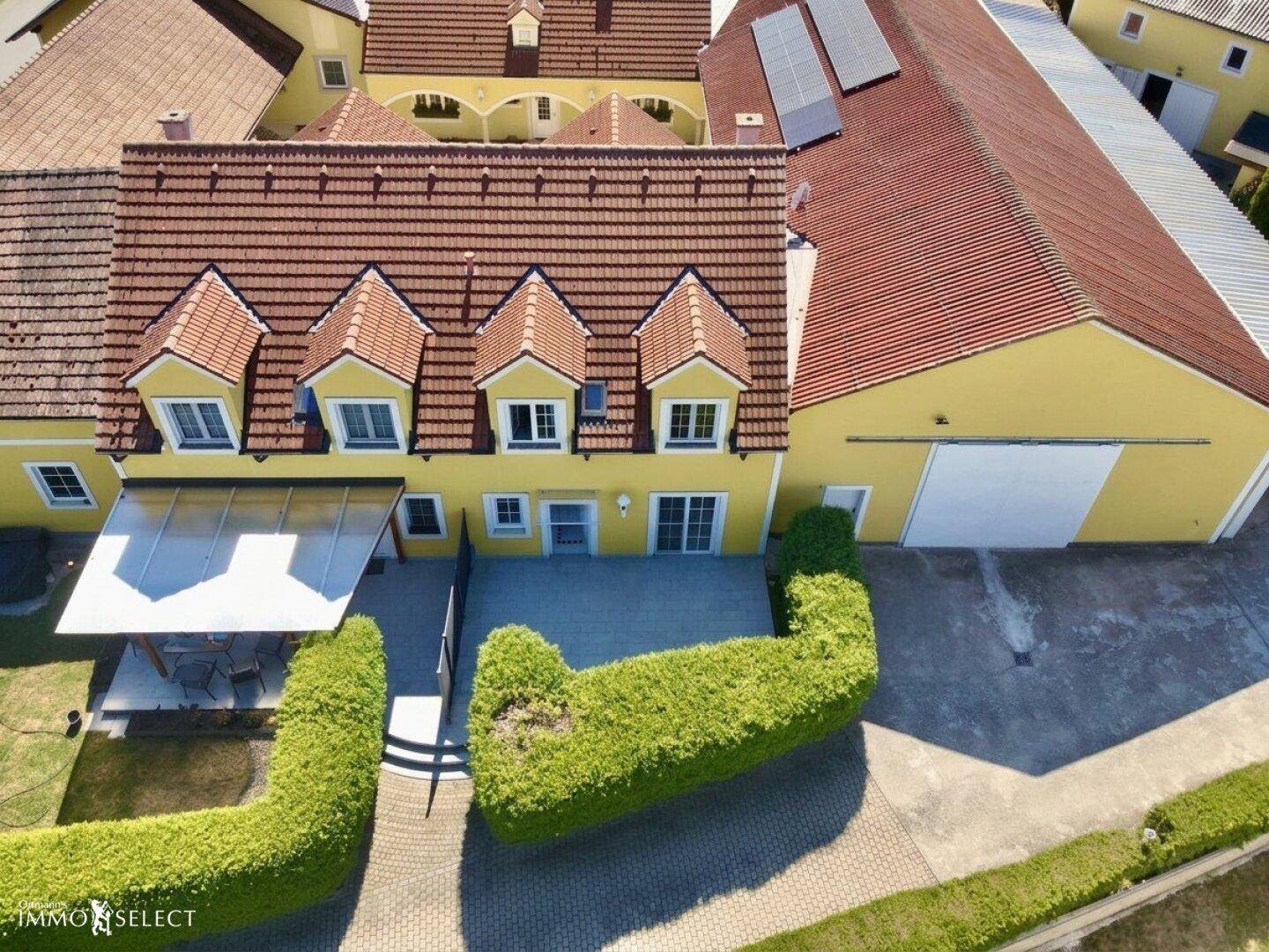 Luftaufnahme des gelben Hauses mit rotem Ziegeldach, Terrasse und Carport.