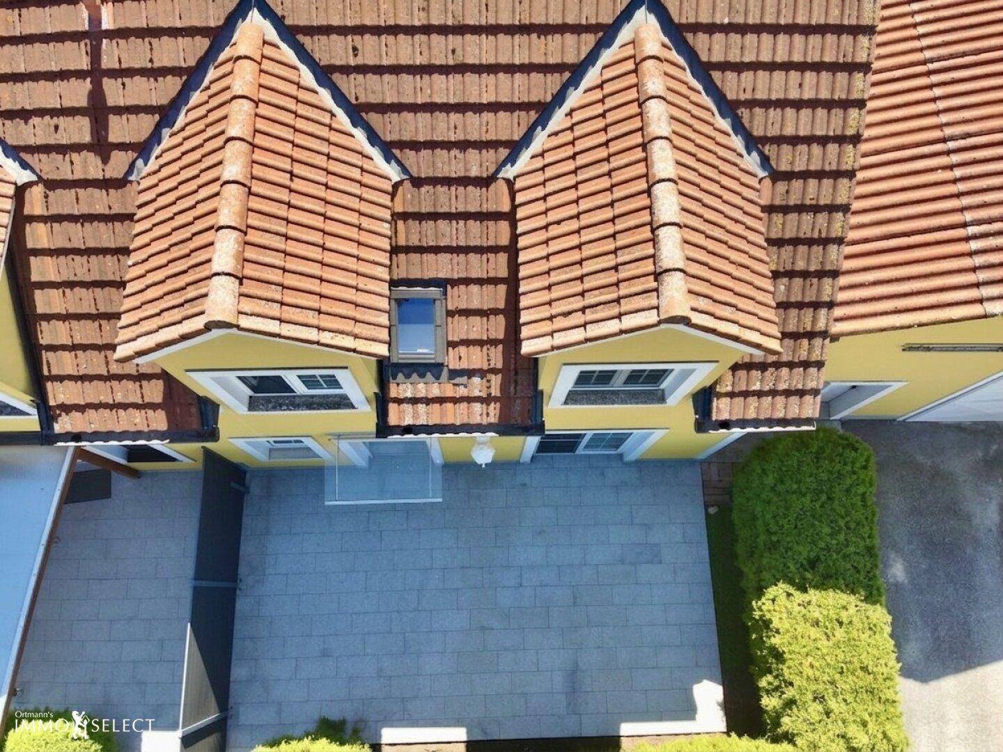Draufsicht auf das gelbe Haus mit rotem Ziegeldach, Terrasse und Carport.