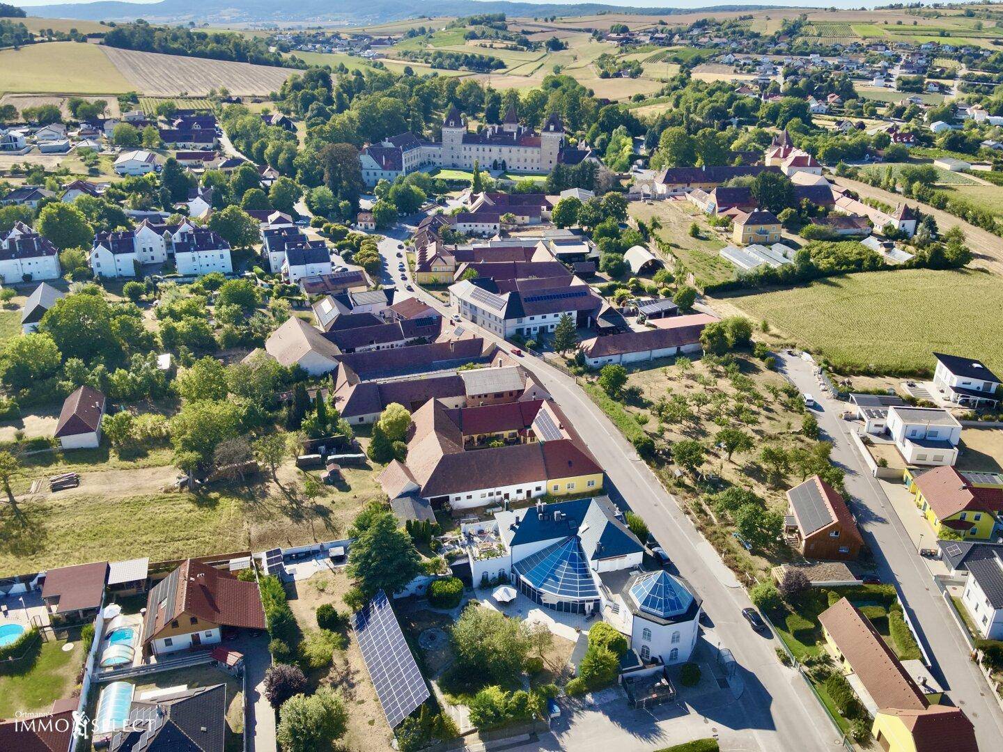 Weitläufige Luftaufnahme des Dorfes mit grüner Landschaft und dem Anwesen im Vordergrund.