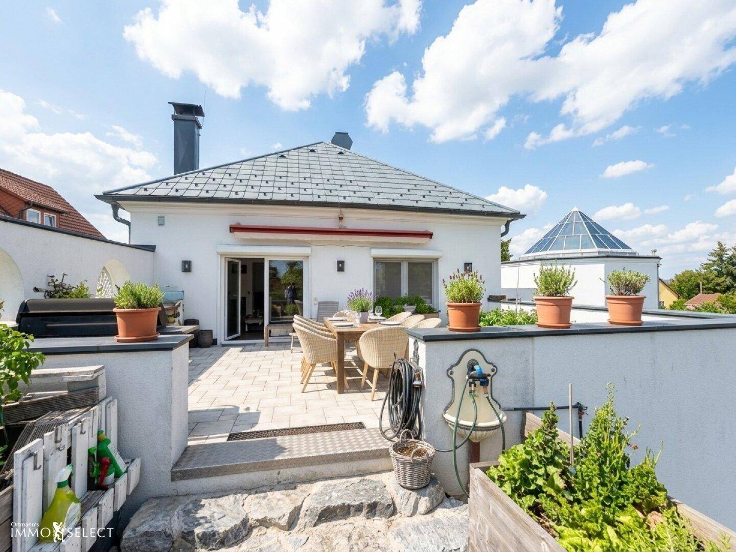 Sonnenterrasse mit Essbereich, Topfpflanzen und einem kleinen Kräutergarten am Haus.