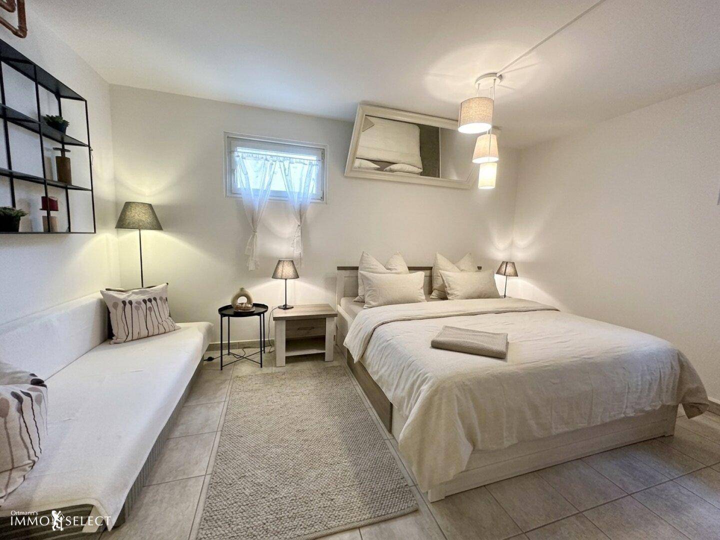 Helles Schlafzimmer mit Doppelbett, Sofa und minimalistischer Einrichtung.