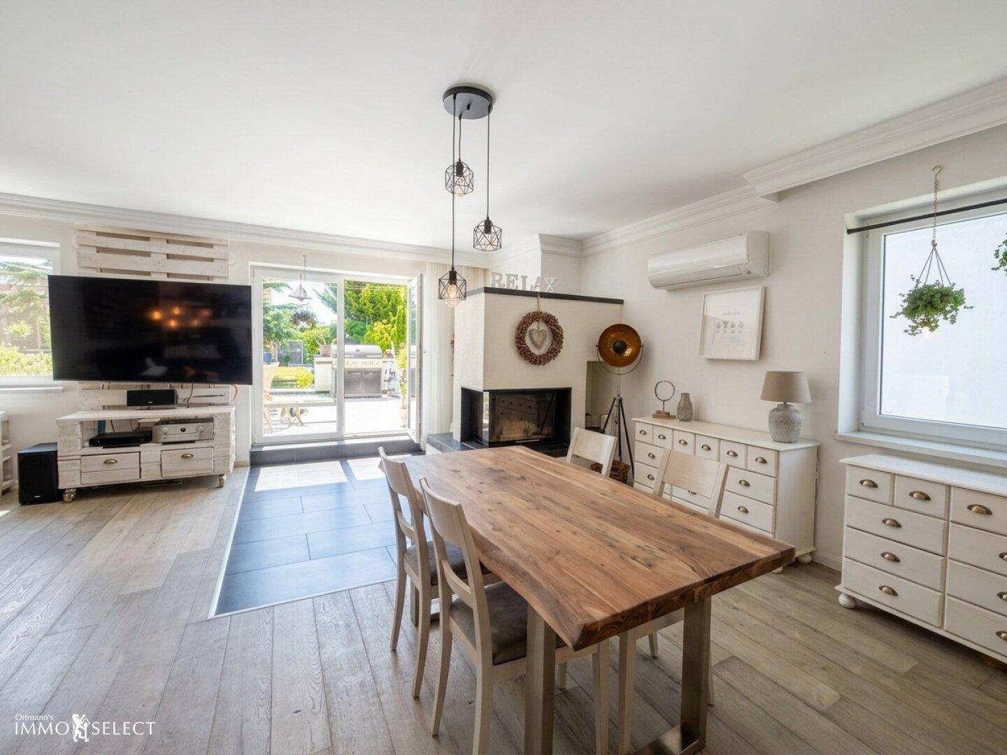 Kombinierter Wohn- und Essbereich mit Holztisch, Kamin und Zugang zu einem Außenbereich.