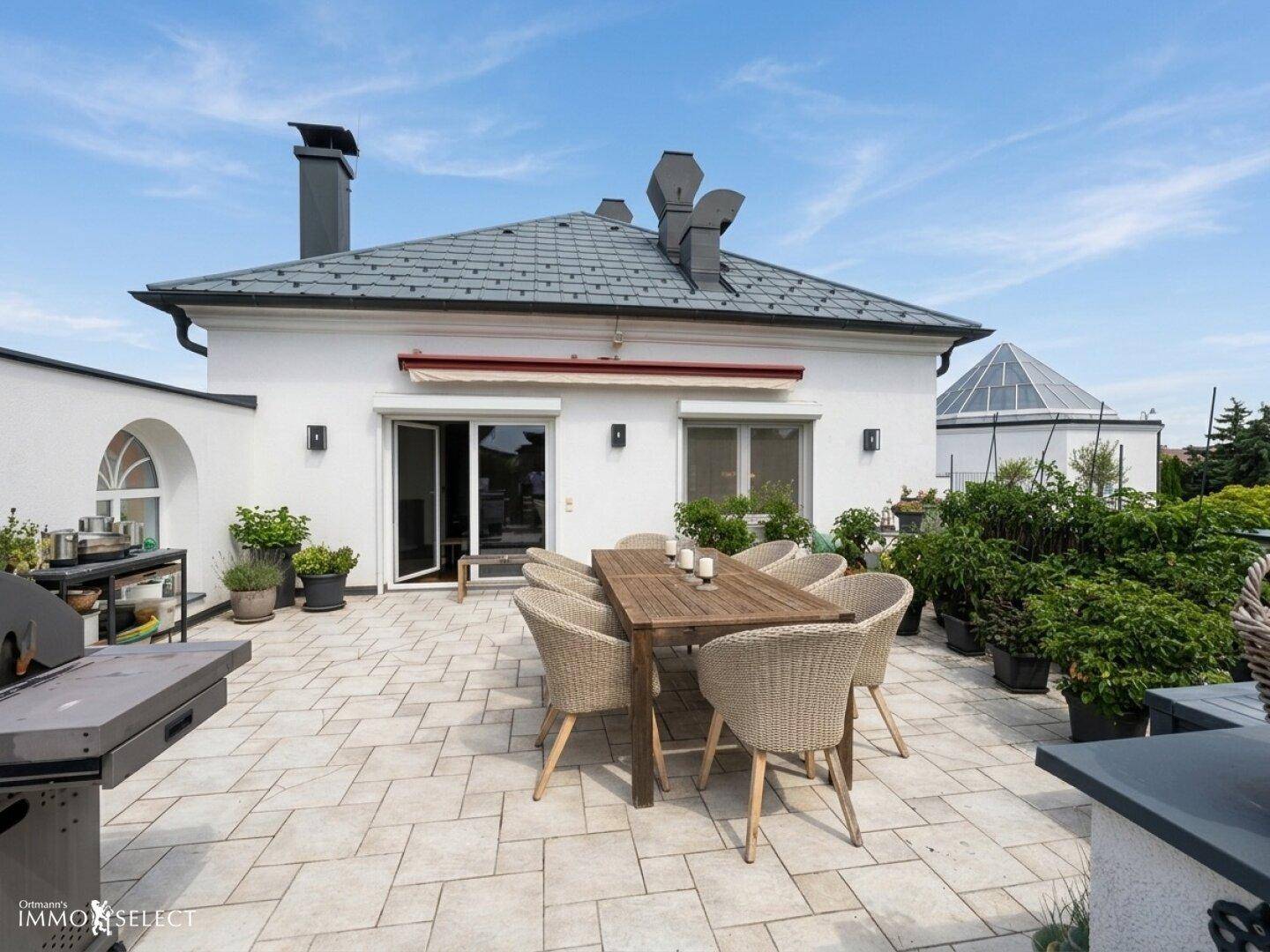Hausfassade mit Terrasse, Esstisch und Blick auf die umliegende grüne Landschaft.
