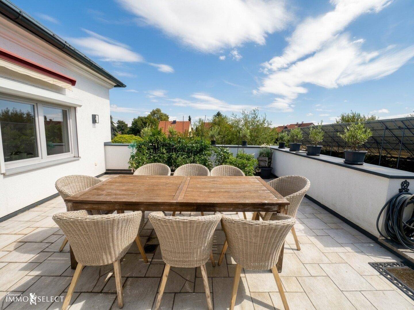 Sonnige Terrasse mit Esstisch, Korbstühlen und Blick auf die grüne Umgebung.
