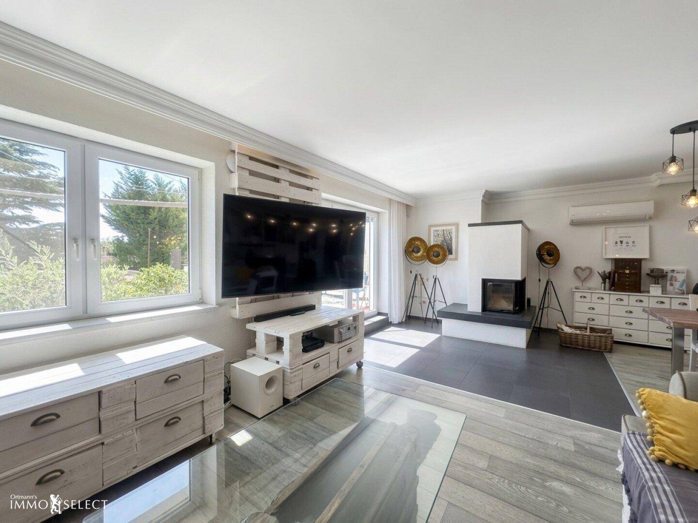 Helles Wohnzimmer mit großem Fernseher, Kamin und Zugang zur Terrasse.