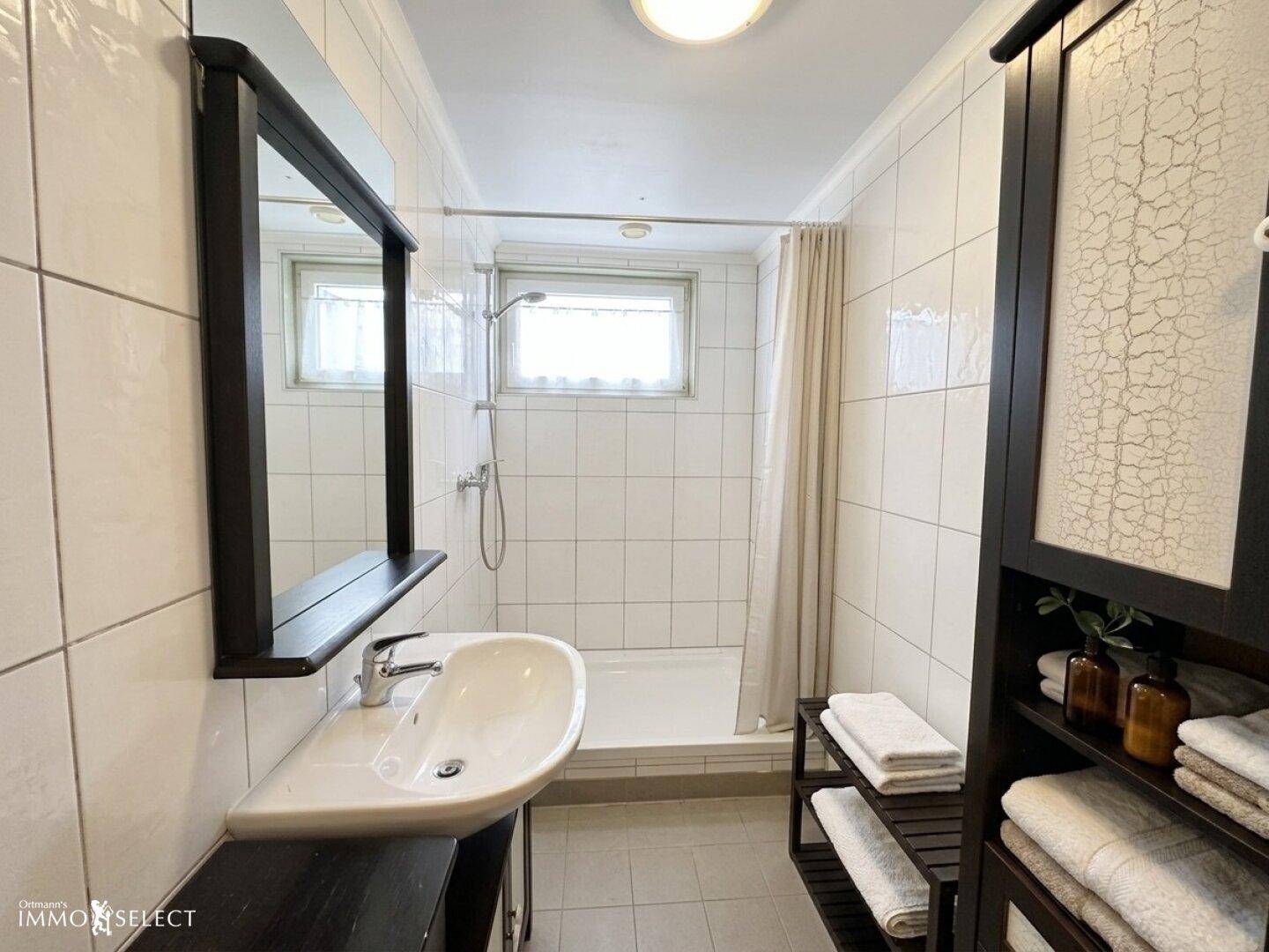 Kleines Badezimmer mit weißen Fliesen, Einzelwaschbecken und Duschbereich mit Fenster.