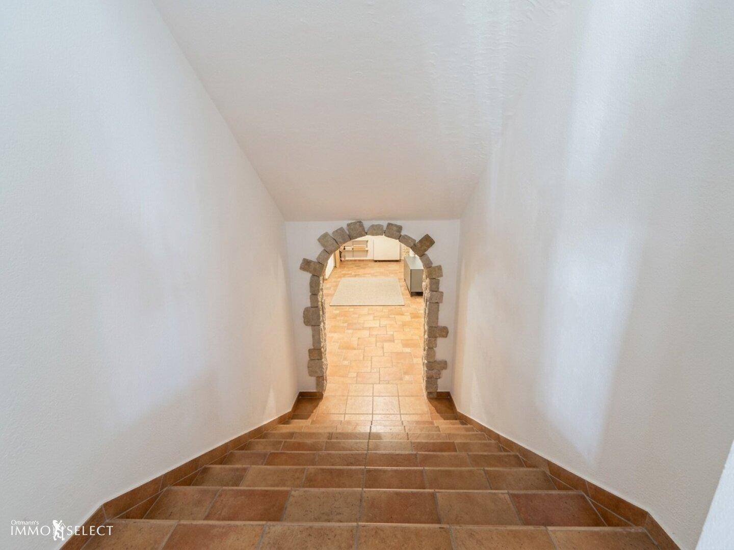 Steile Treppe mit Terrakottafliesen und einem rustikalen Steinbogen am unteren Ende.