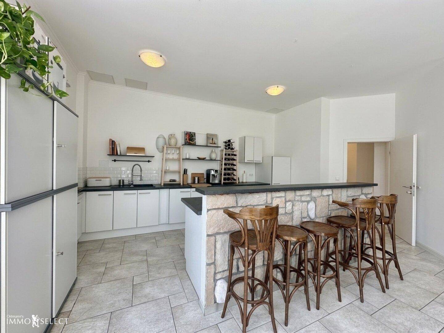 Moderne Küche mit weißer Einbauküche, Steinverkleidung und Frühstücksbar.