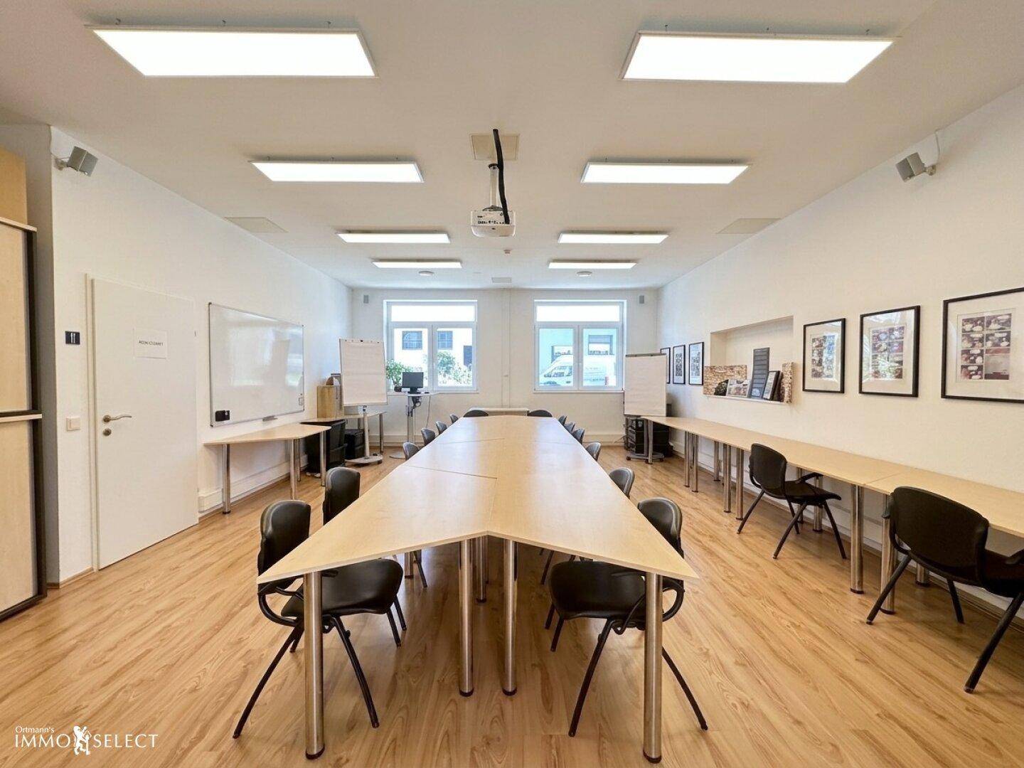 Heller Konferenzraum mit langem Tisch, Stühlen, Whiteboards und einem Beamer.