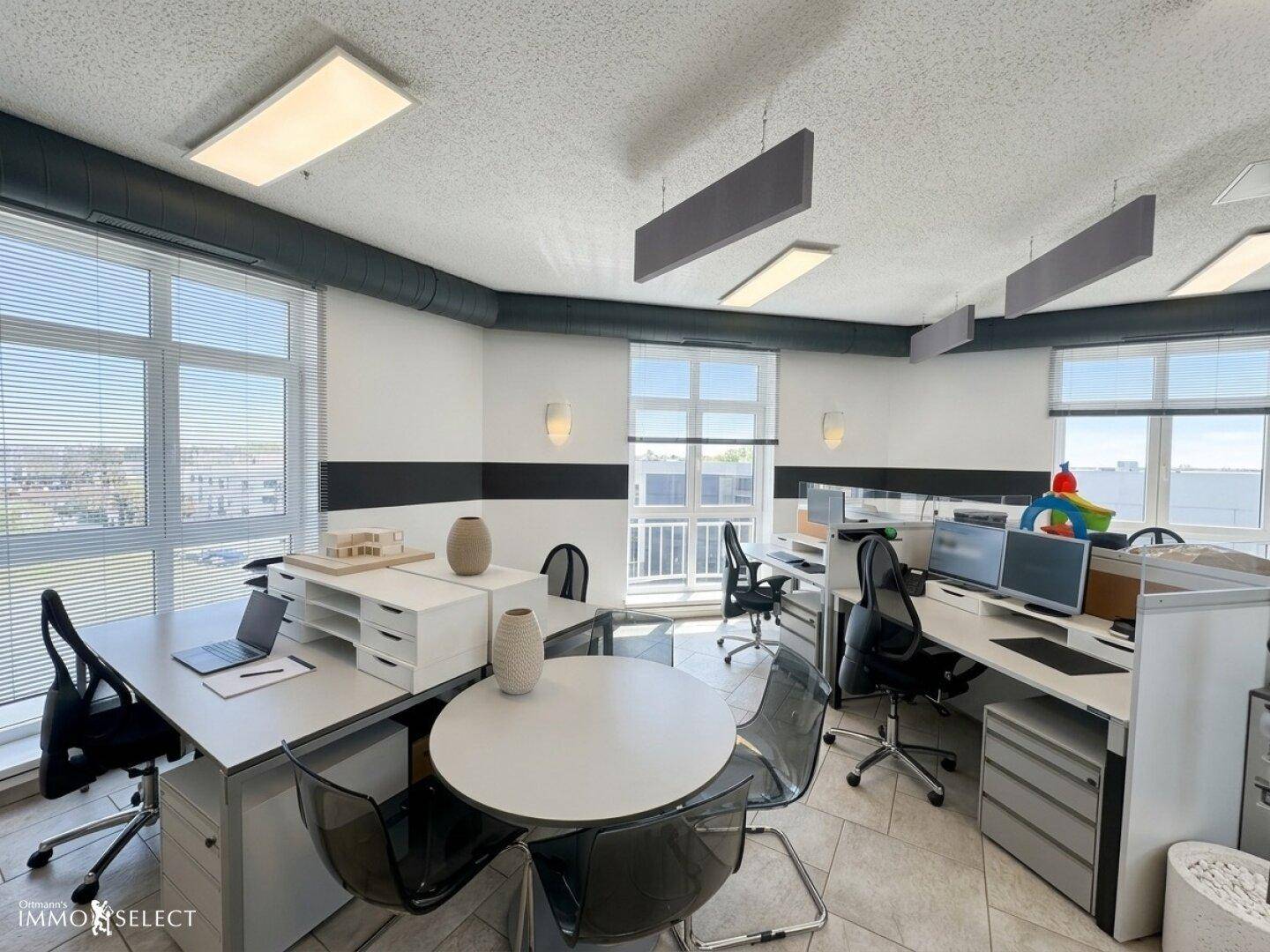 Modernes Büro mit mehreren Arbeitsplätzen, großen Fenstern und Blick auf die Umgebung.