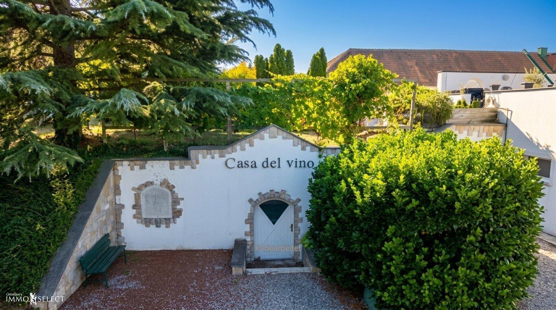 Kleines Gebäude mit der Aufschrift "Casa del vino" umgeben von Bäumen und Weinreben.