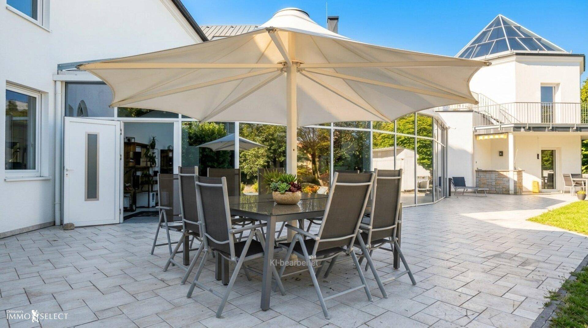 Große gepflasterte Terrasse mit Esstisch, Sonnenschirm und Blick auf das moderne Gebäude.