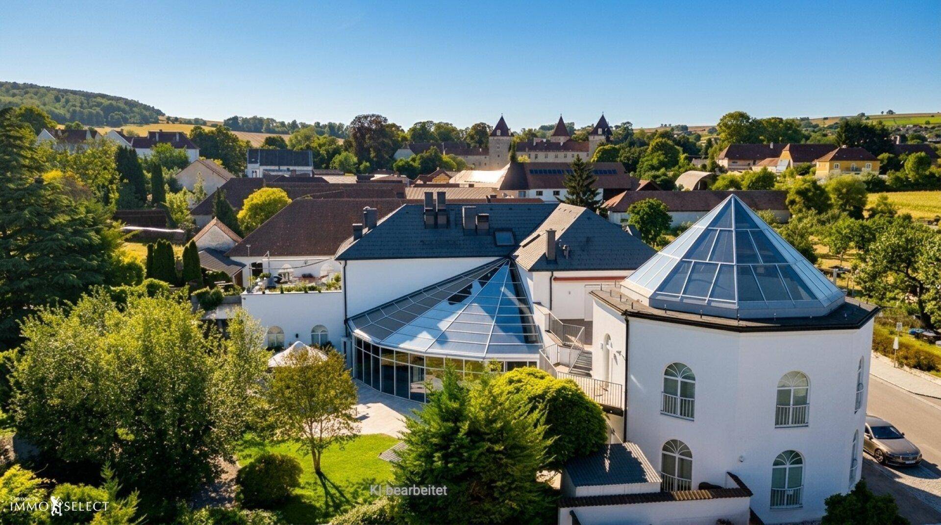Luftaufnahme eines weitläufigen Gebäudekomplexes mit Glasdach und umgebender grüner Landschaft.