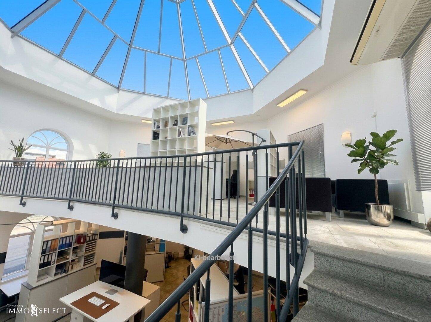 Heller Empfangsbereich mit Glasdach, Galerie und Treppe in einem modernen Bürogebäude.