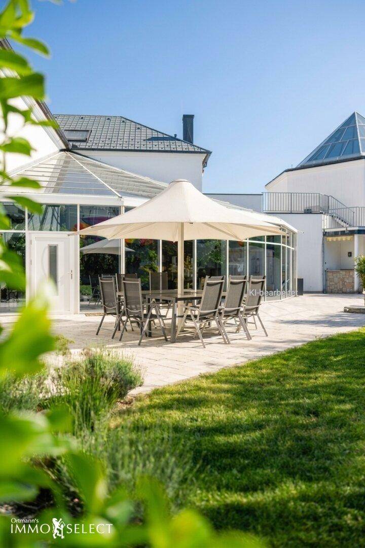 Sonniger Terrassenbereich mit Esstisch und Sonnenschirm, umgeben von gepflegtem Rasen und Pflanzen.