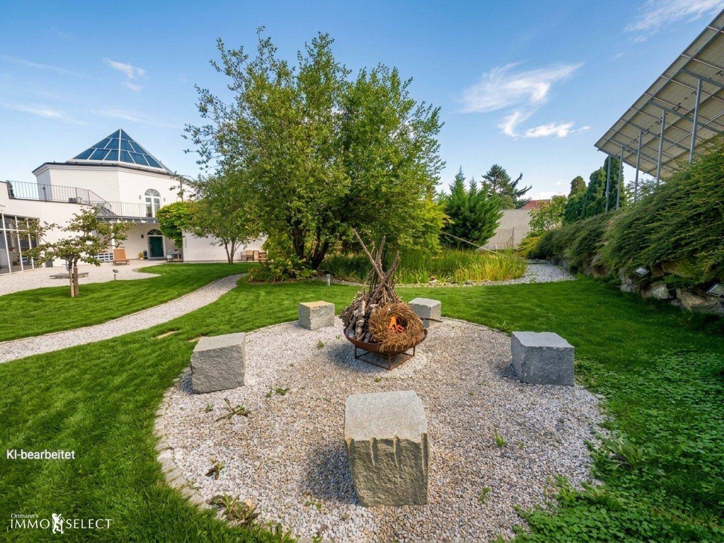 Gepflegter Garten mit Feuerstelle, Steinbänken, Rasenflächen und einem Gebäude im Hintergrund.