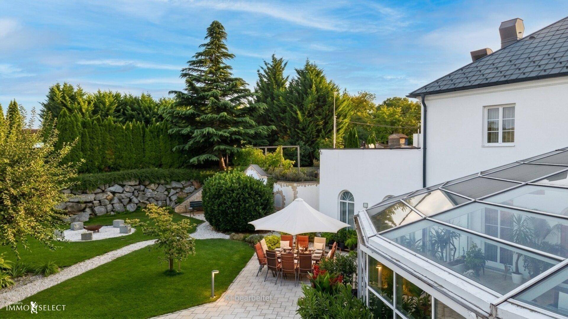 Gepflegter Garten mit Rasenfläche, Steingarten und einer möblierten Terrasse unter einem Sonnenschirm.