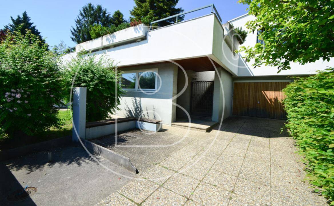 Modernes Haus mit gepflasterter Auffahrt, Garage und viel Grün in der Umgebung.