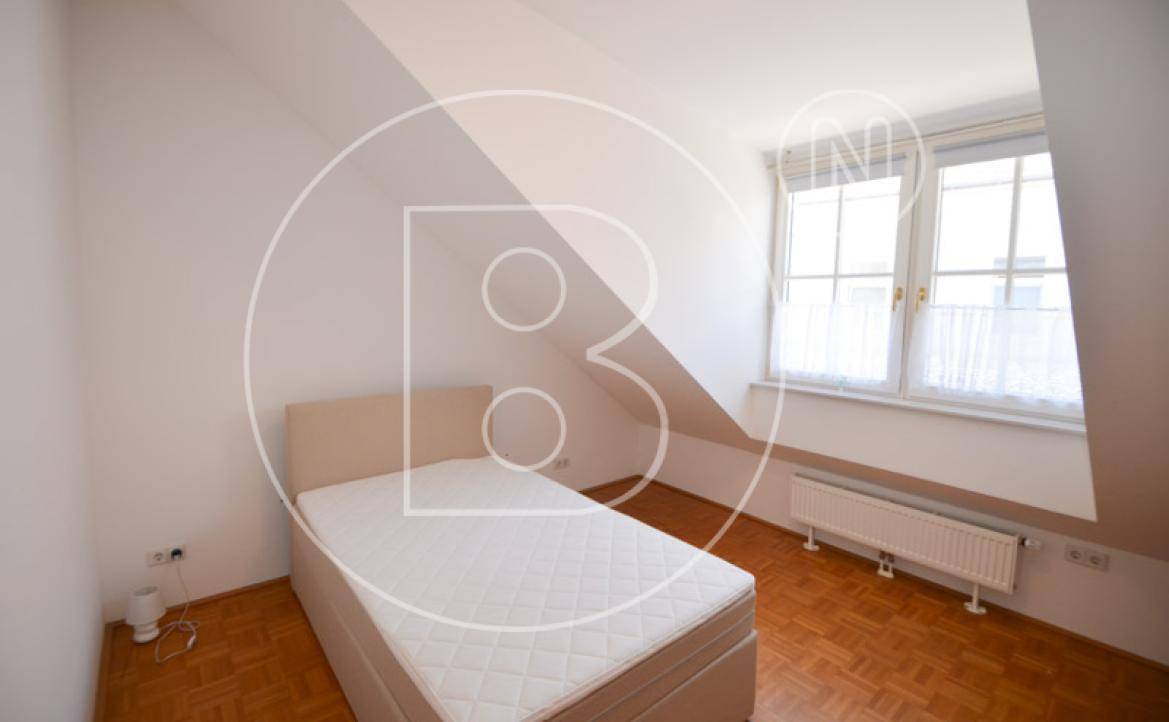 Helles Schlafzimmer im Dachgeschoss mit schrägen Wänden, Einzelbett und Fenster.