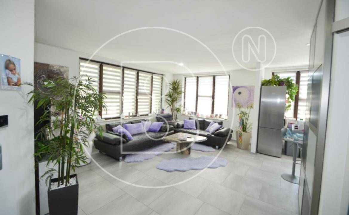 Geräumiges Wohnzimmer mit bequemen Sofas, Fliesenboden und vielen Fenstern.