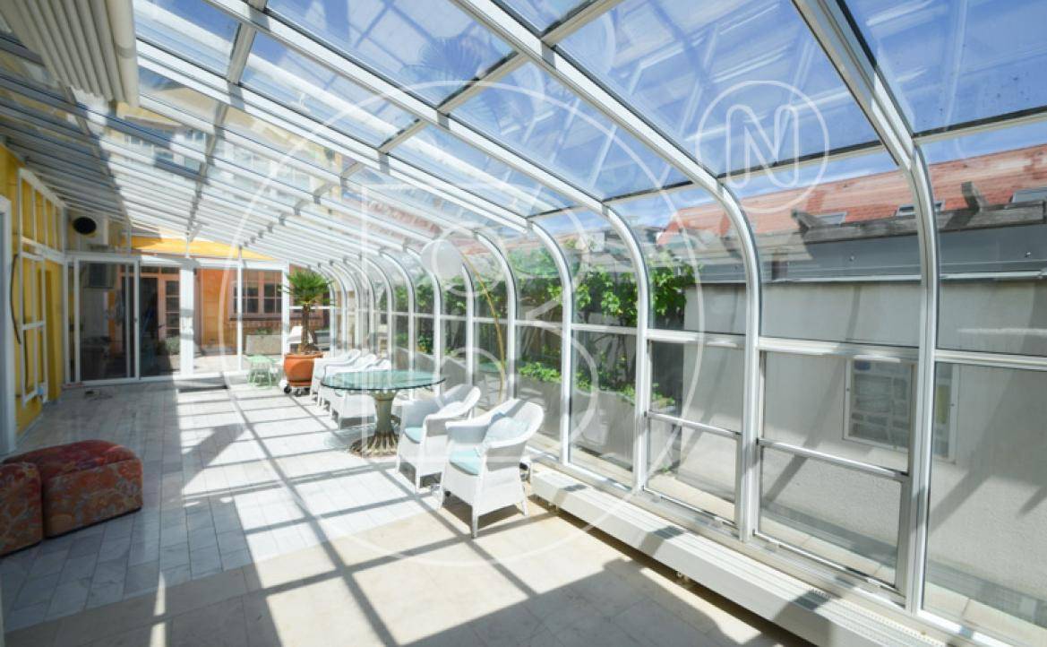 Heller Wintergarten mit Glasdach, Sitzgelegenheiten und Blick ins Grüne.