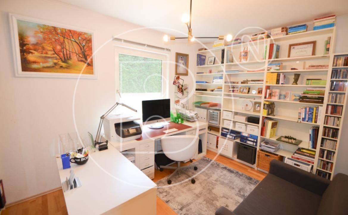 Funktionales Arbeitszimmer mit großem Bücherregal, Schreibtisch und Blick ins Grüne.