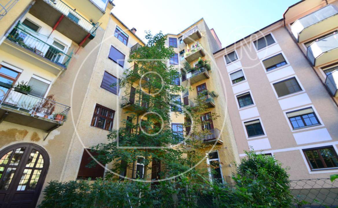 Rückansicht eines Wohngebäudes mit mehreren Balkonen und üppiger Vegetation im Innenhof.