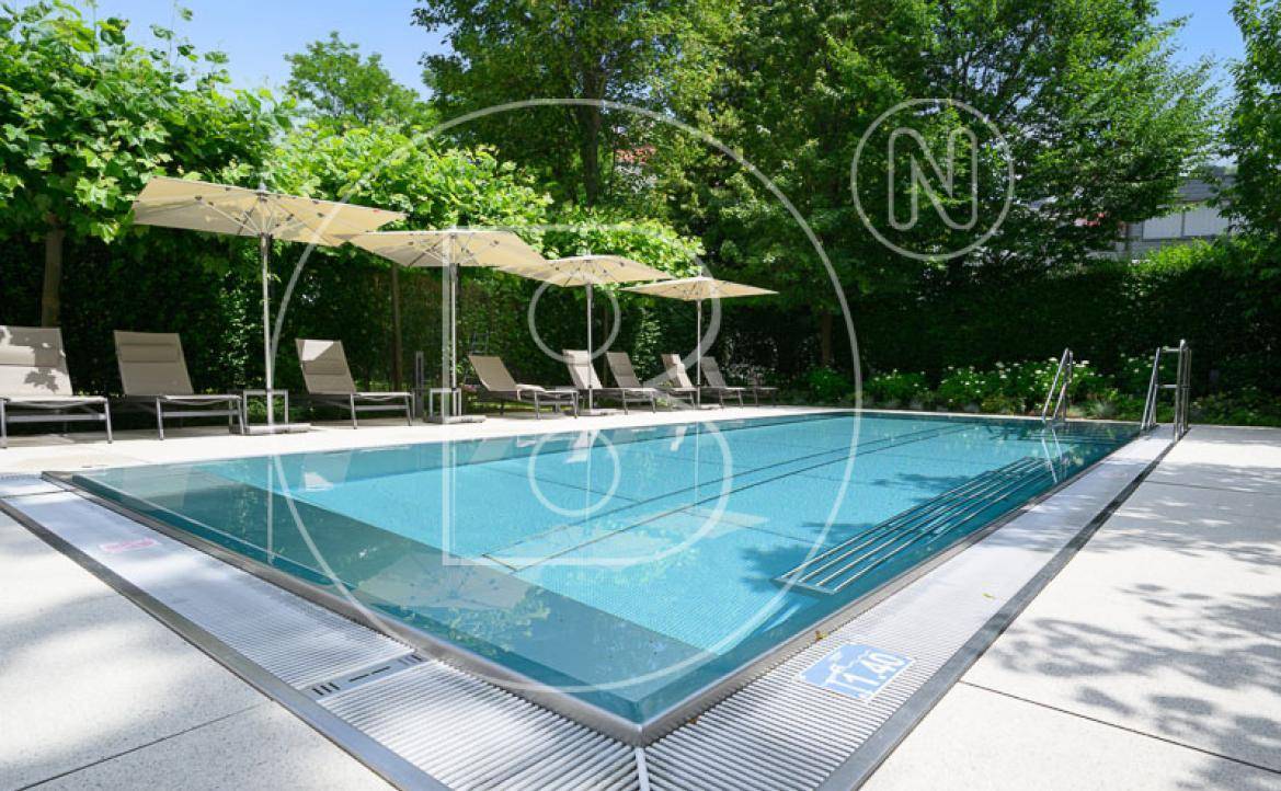 Gepflegter Außenpoolbereich mit Sonnenliegen und Sonnenschirmen, umgeben von Grün.
