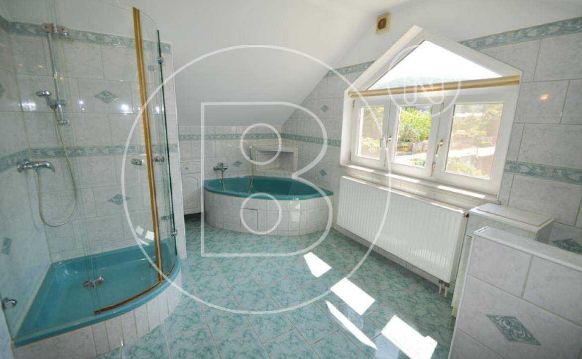 Badezimmer mit Eckbadewanne, Duschkabine und hellblauen Fliesen im Dachgeschoss.