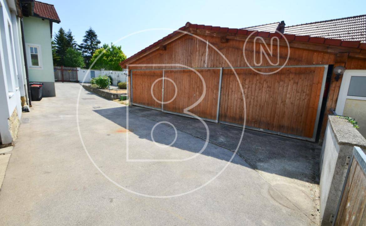 Gepflasterte Einfahrt neben einer Holzgarage mit Blick auf das Grundstück.
