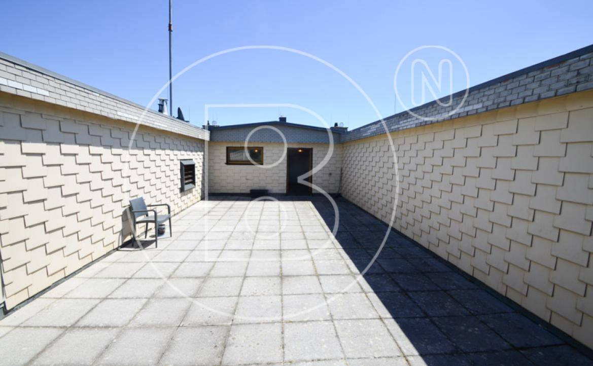 Weitläufige Dachterrasse mit Fliesenboden und Zugang zu einem kleinen Gebäude.