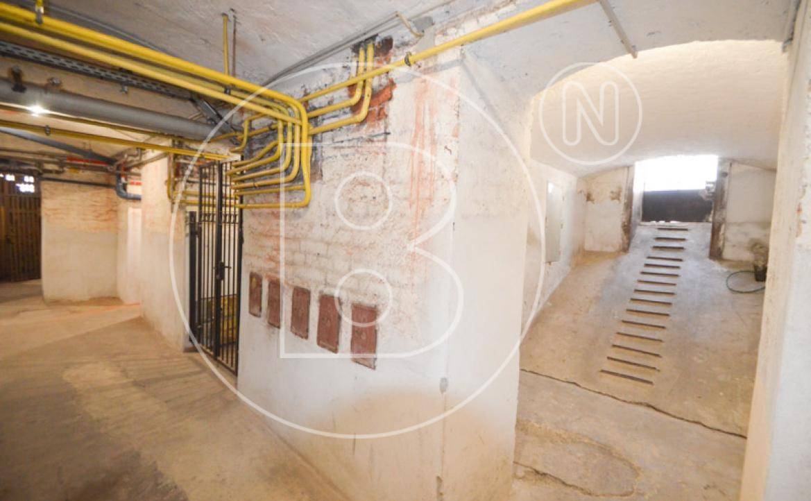 Geräumiger Kellerraum mit sichtbaren Rohrleitungen, Betonboden und einer Rampe, die zu weiteren Bereichen führt.