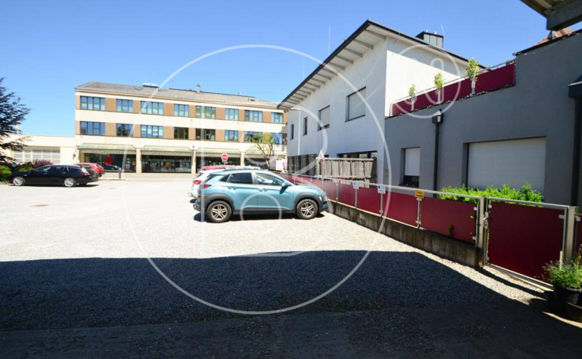 Gebäudekomplex mit Parkplatz und Blick auf ein größeres Gebäude gegenüber der Straße.