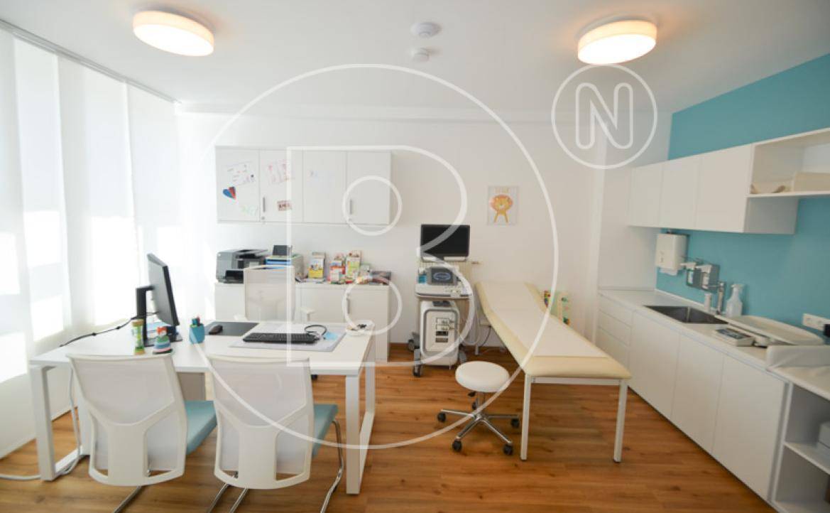 Modernes Behandlungszimmer mit Schreibtisch, Untersuchungsliege und blauen Akzenten.
