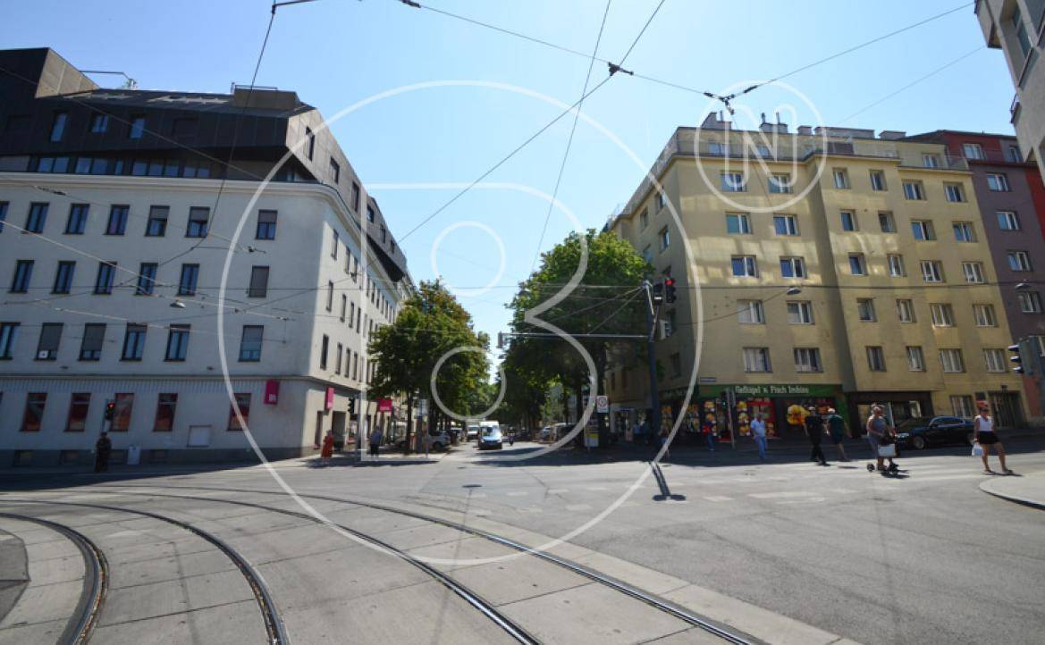 Weitläufige Straßenkreuzung mit Straßenbahnschienen, umgeben von städtischen Gebäuden und Bäumen.