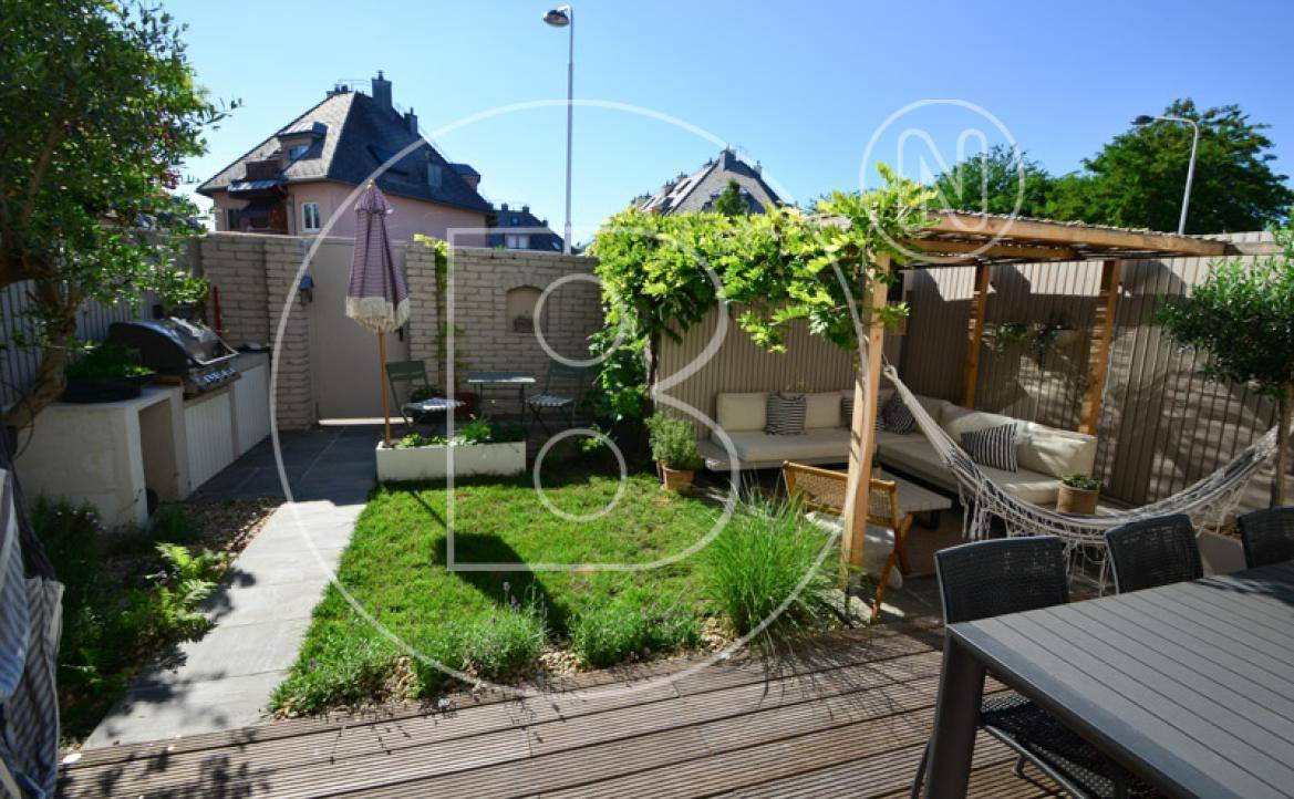 Sonniger Gartenbereich mit Holzterrasse, Grillplatz und gemütlicher Lounge-Ecke.