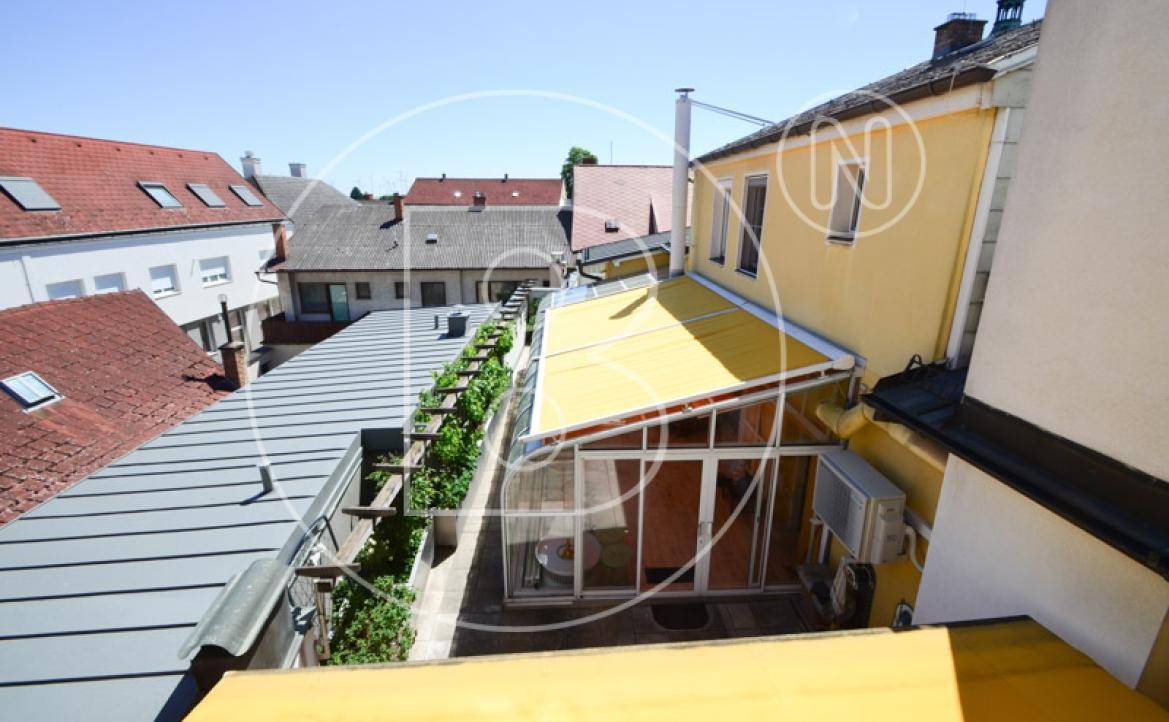 Dachansicht des Gebäudes mit Terrassenbereich und Wintergarten unter blauem Himmel.