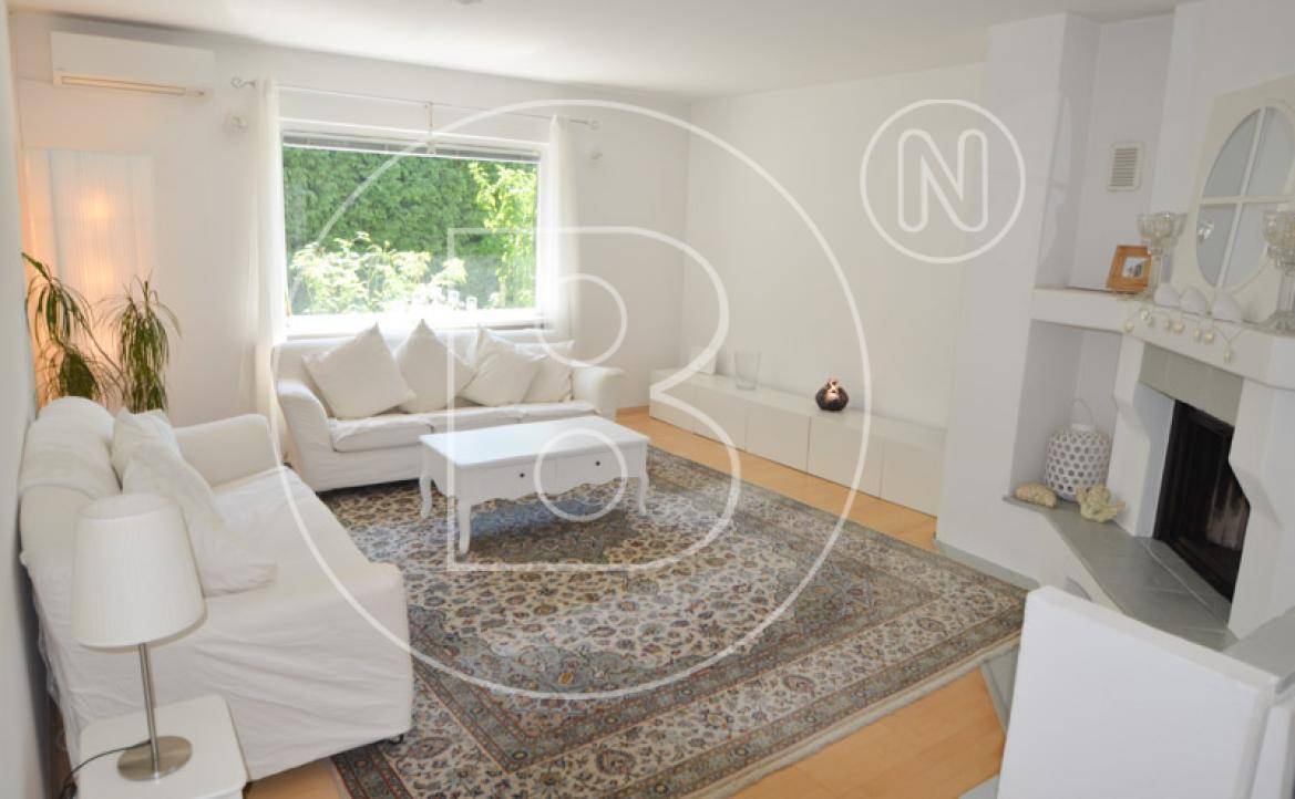 Helles Wohnzimmer mit Kamin, zwei weißen Sofas und Blick auf den grünen Garten.
