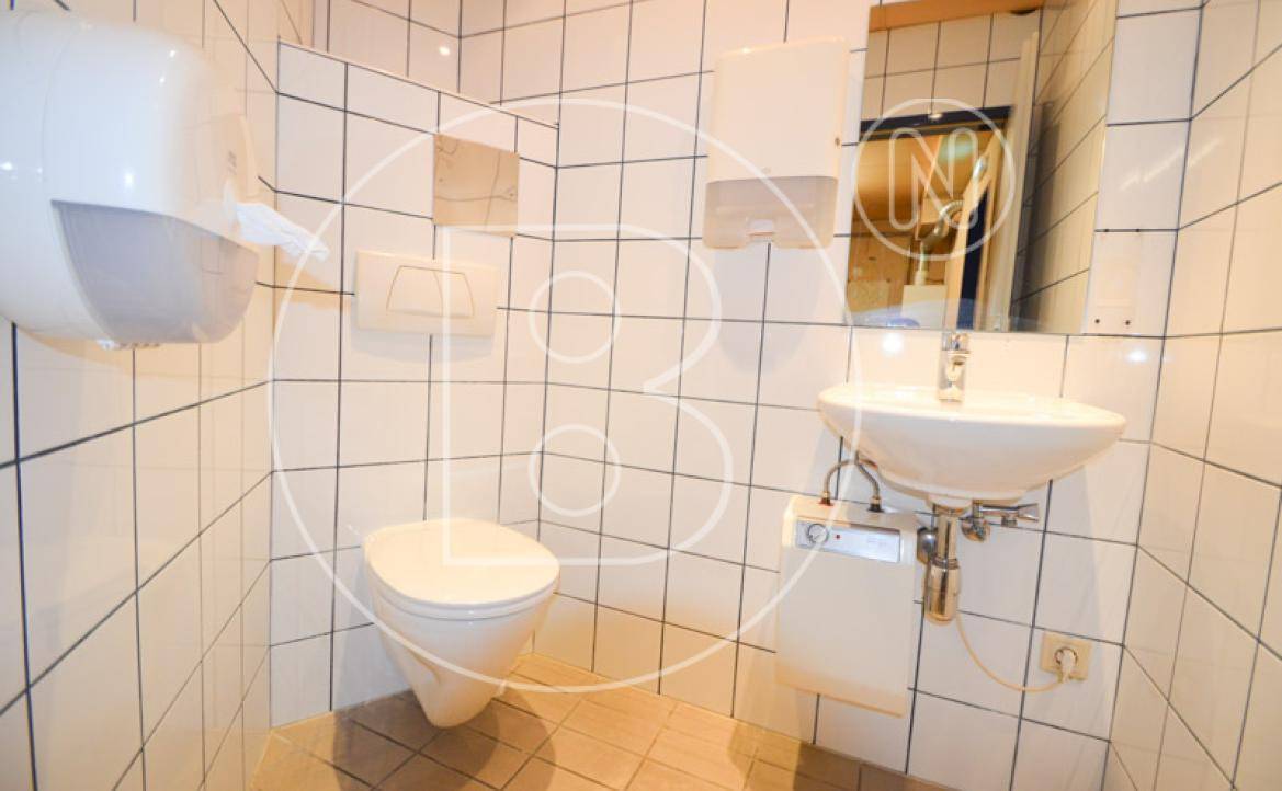 Saubere und funktionale Toilette mit weißen Fliesen, Wand-WC und Waschbecken.
