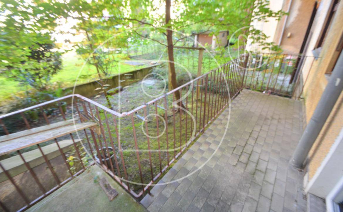 Ein kleiner Balkon mit Metallgeländer und Blick auf einen grünen, bewachsenen Hinterhof.