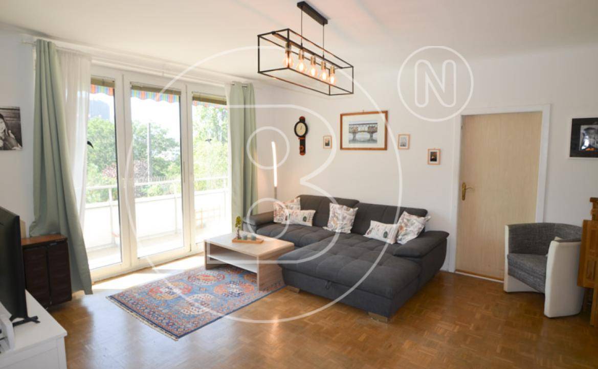 Heller Wohnbereich mit großem Sofa, Teppich und Zugang zum sonnigen Balkon für entspannte Stunden.