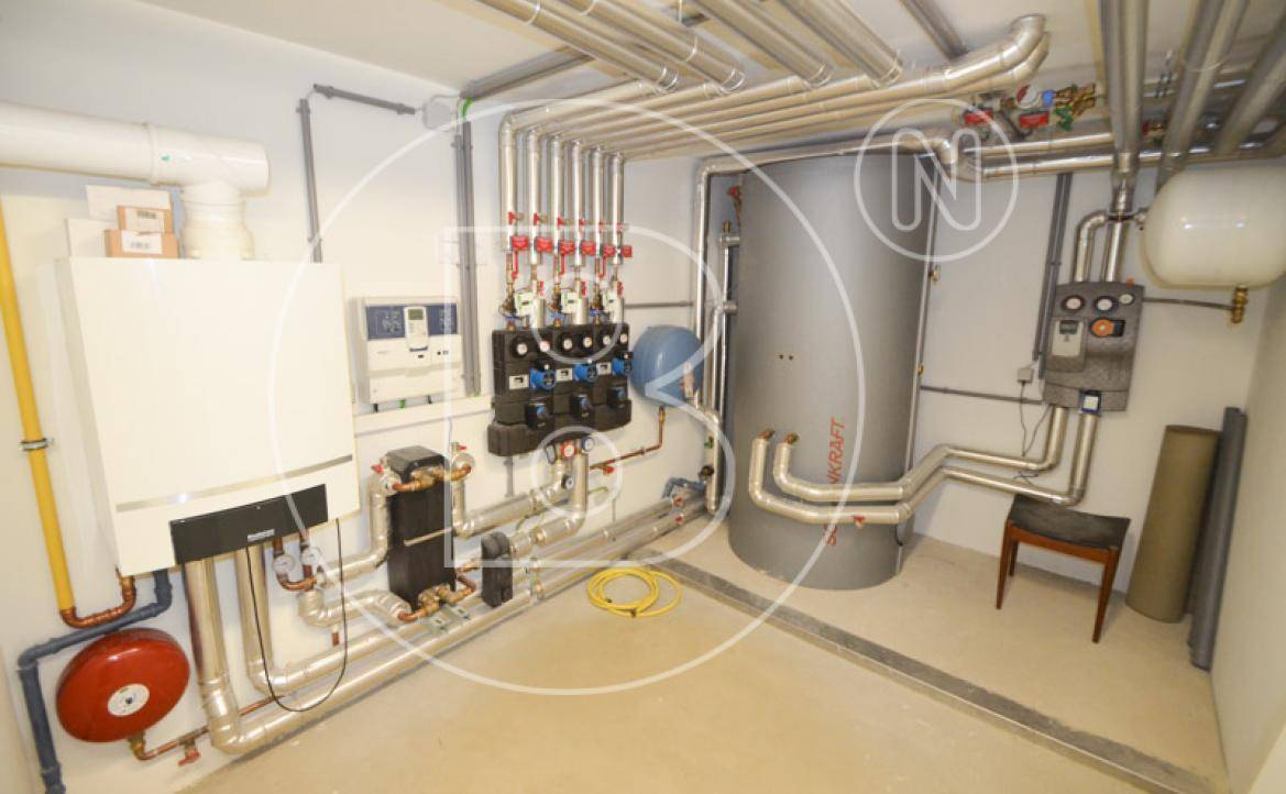 Technikraum mit Heizungsanlage, Warmwasserspeicher und zahlreichen Rohrleitungen.
