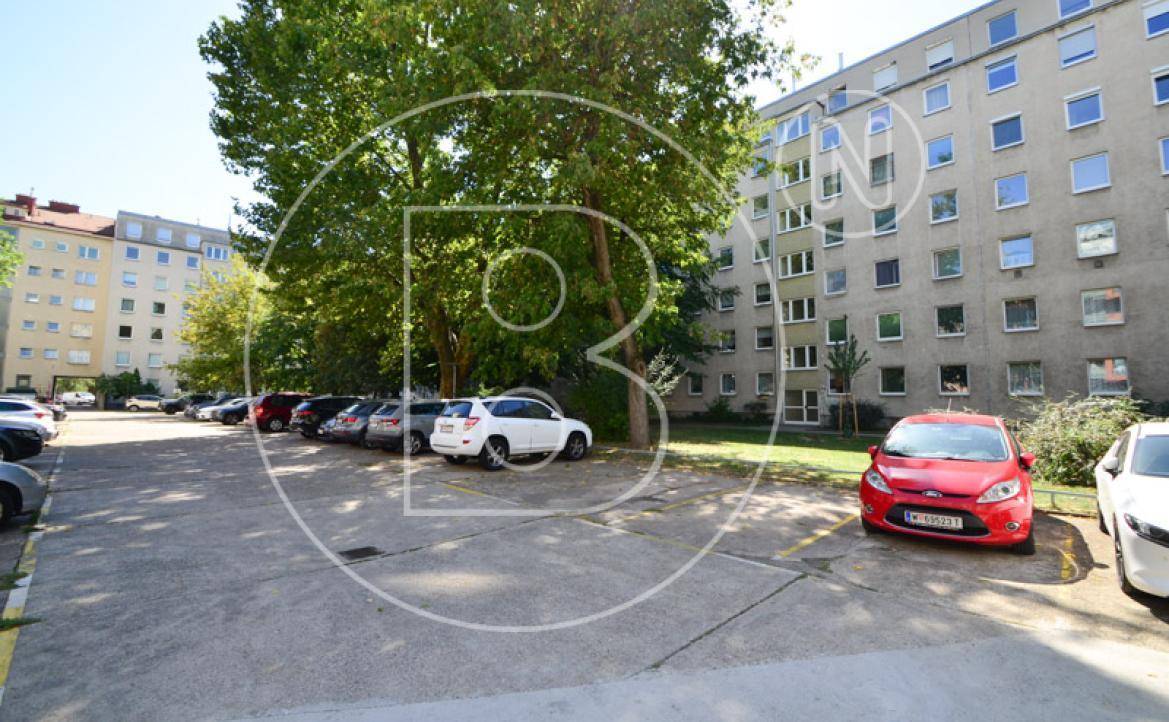 Außenparkplätze vor einem Wohngebäude mit Bäumen und geparkten Autos.