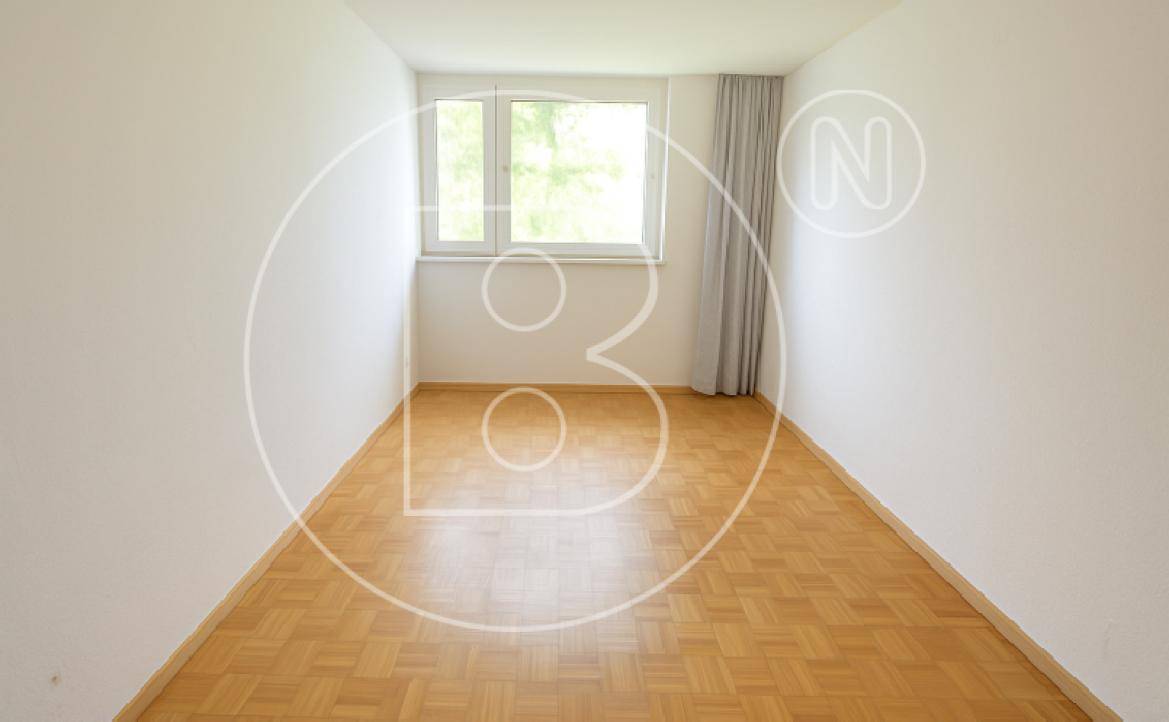 Helles Schlafzimmer mit Parkettboden und großem Fenster, das viel Tageslicht hereinlässt.
