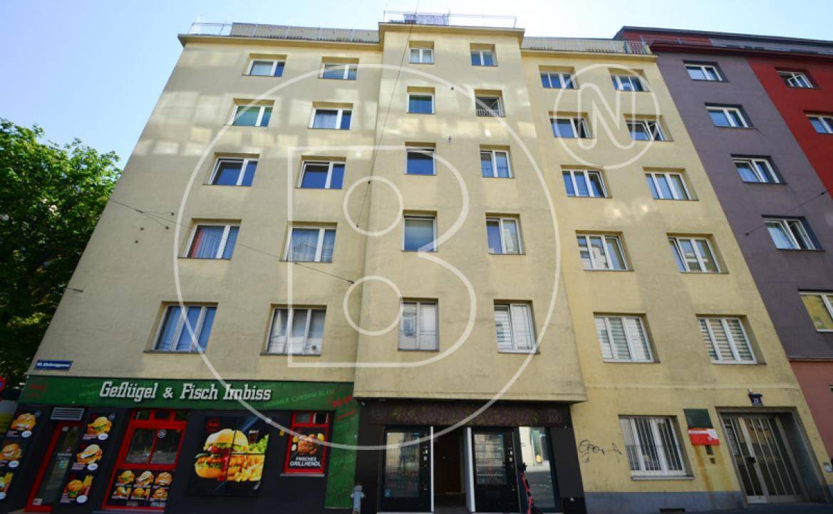 Mehrstöckiges Gebäude mit gelber Fassade und einem Imbissgeschäft im Erdgeschoss an einer belebten Straße.