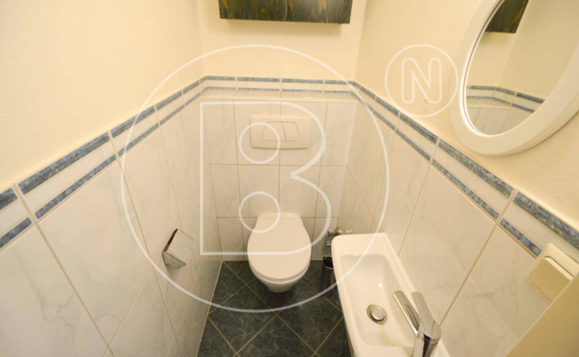 Kleines Gäste-WC mit Toilette, Handwaschbecken und weiß-blauen Fliesen an den Wänden.