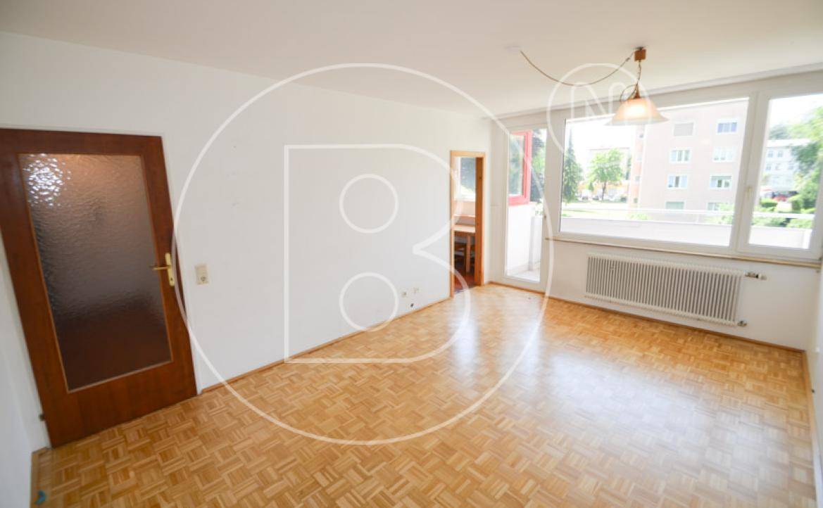 Helles Wohnzimmer mit Parkettboden, großem Fenster und Zugang zu einem Balkon.