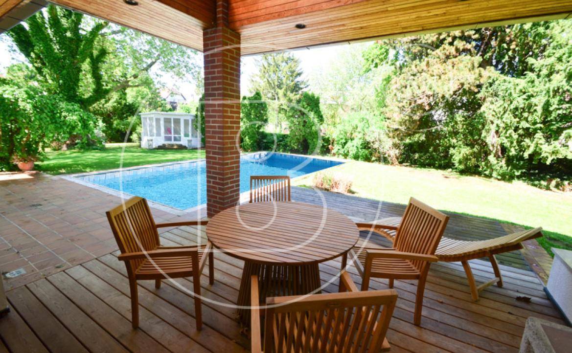 Überdachte Holzterrasse mit Esstisch und Stühlen, direkt am Swimmingpool gelegen.
